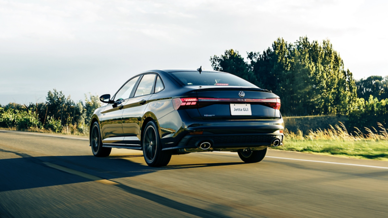 Rear view of the Jetta GLI driving on an open road with warm sunset lighting. 