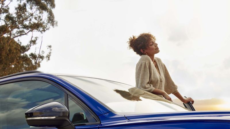 Vista di una ragazza appoggiata allo sportello di una vettura Volkswagen parcheggiata.