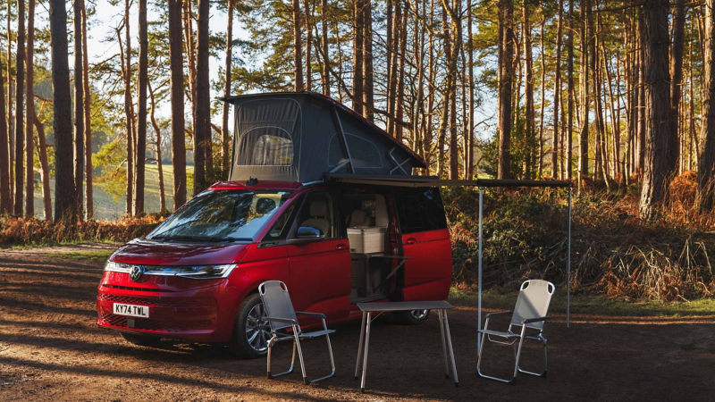 Photo of a California parked in a forest with the awning and dining accessories deployed.