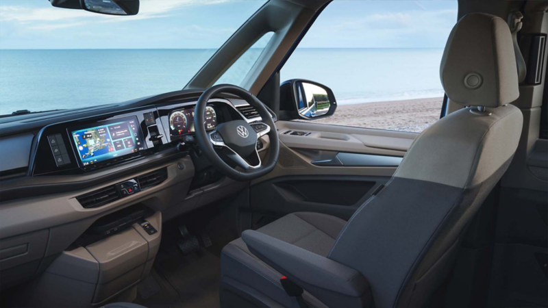 Photo showing the interior cockpit of a VW camper, against an ocean background. 