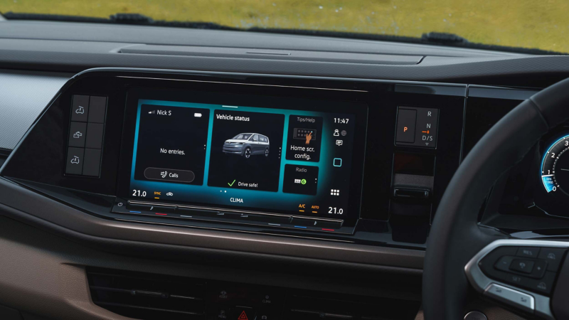 Photo of a California parked on a beach with two people sat in front of it eating.