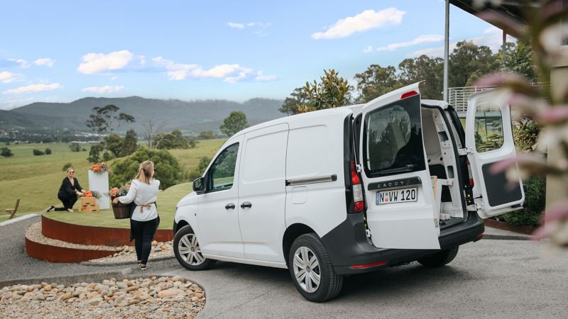 white Volkswagen Caddy Cargo parked in a driveway with women carrying flowers