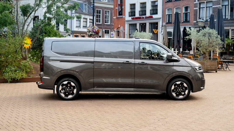 Grijze Volkswagen e-Transporter geparkeerd op een plein in een historische binnenstad.
