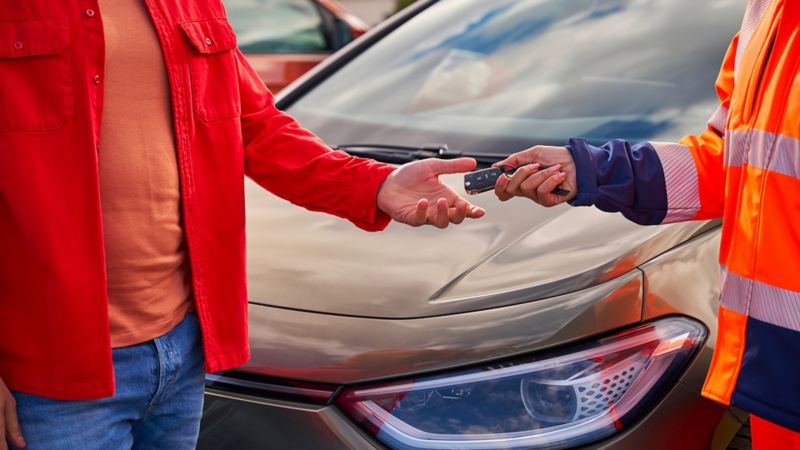 Customer takes car keys from VW service employee, in the background a VW car