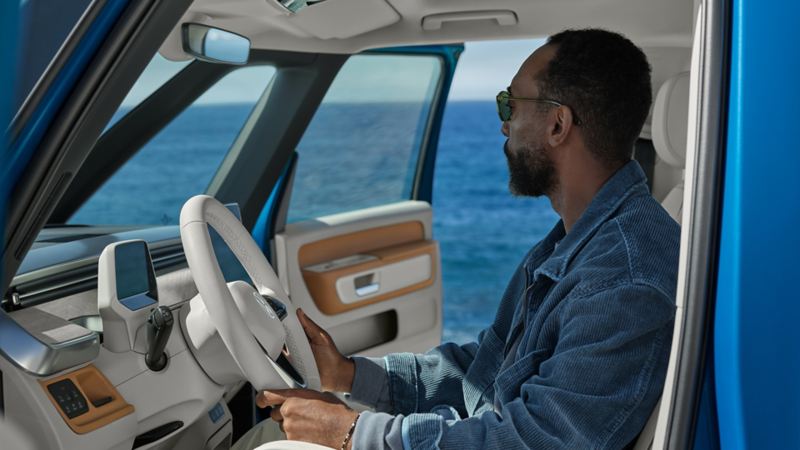 The VW ID. Buzz 2025 is parked by the beach, with two people loading a surfboard into the back.