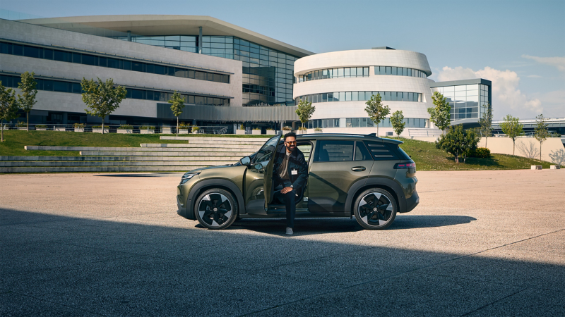 Ein Mann steigt aus der Fahrertür eines VW ID. Cross, der vor einem modernen, mehrstöckigen Firmengebäude steht.