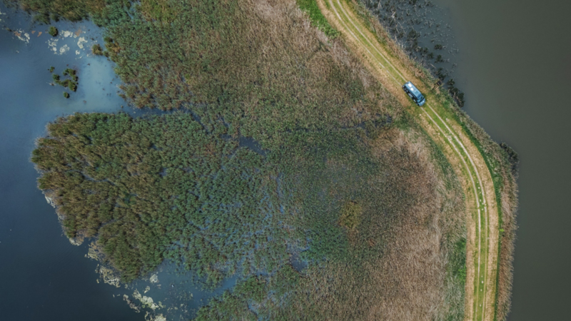 Vue aérienne d’un California Camper roulant sur une route qui traverse un plan d’eau comme un ponton.