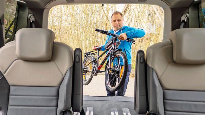 Il padre mette una bicicletta nel bagagliaio del Multivan.