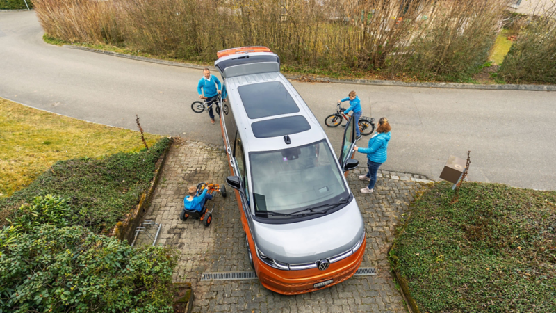Der Multivan steht vor der Garage, von der Familie umgeben.