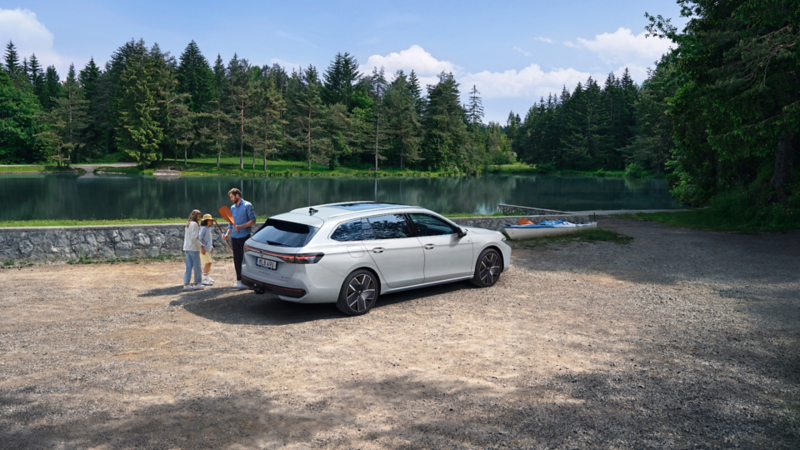  En vit Passat står parkerad vid en sjö. En man och två barn står utanför bilen med en paddel i handen