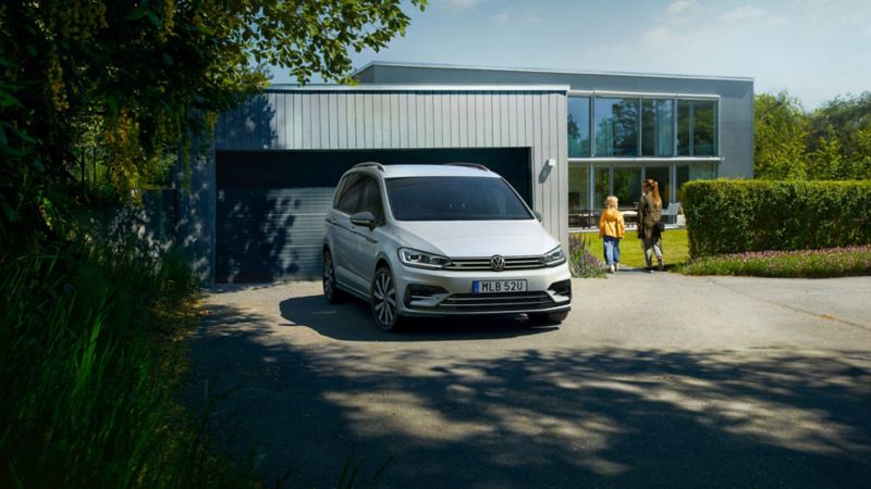 VW Touran parkerad framför en garageport, familj i bakgrunden
