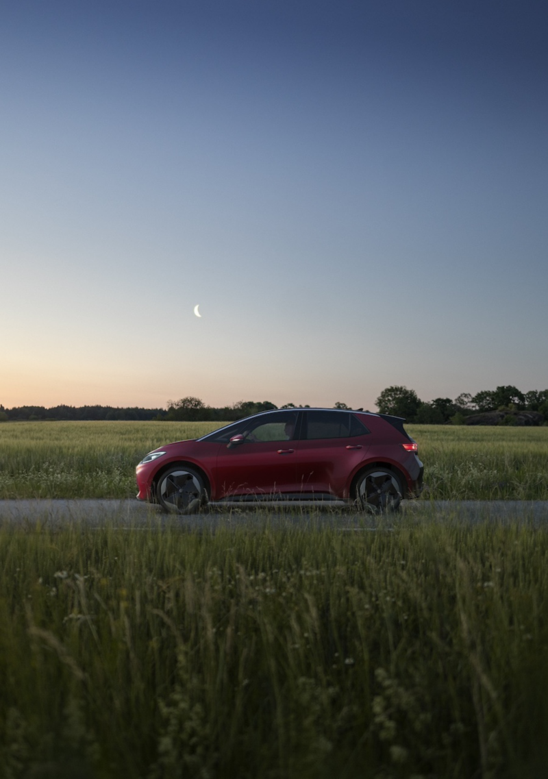 En röd VW ID.3 står på en väg kantad av grönskande ängar, sedd från sidan