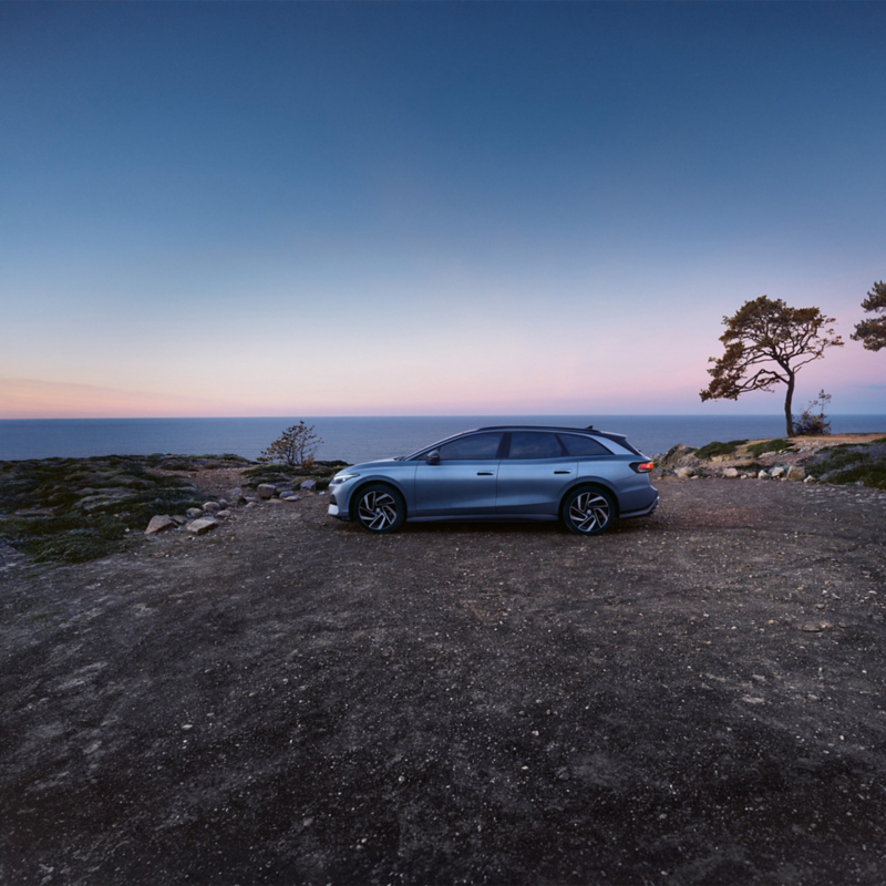 Blåmetallic ID.7 Tourer från sidan med havet i gryningen i bakgrunden