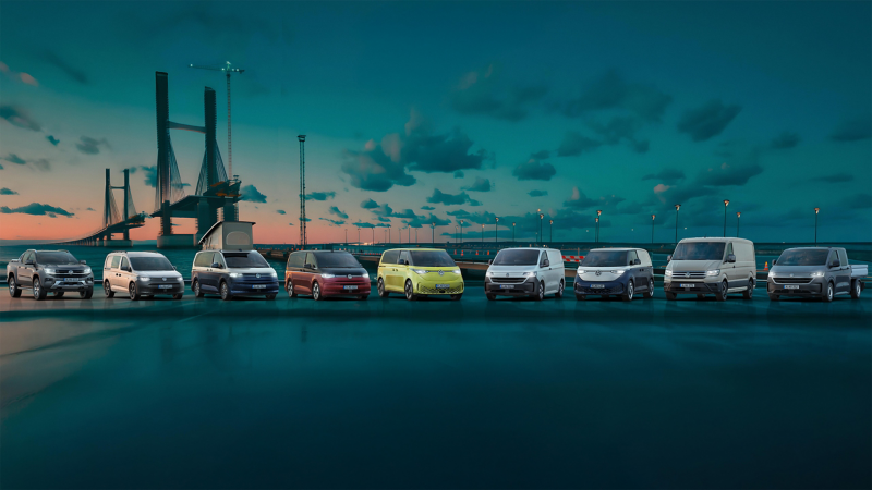 Eine Flotte von VW Nutzfahrzeugen steht vor einer großen, sich im Bau befindenden Brücke.