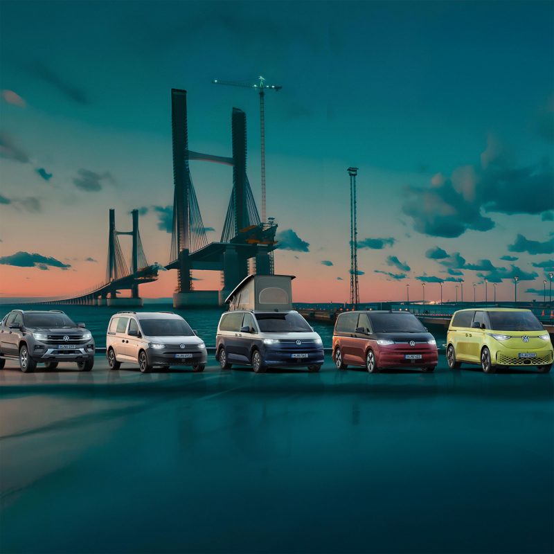 Eine Flotte von VW Nutzfahrzeugen steht vor einer großen, sich im Bau befindenden Brücke.