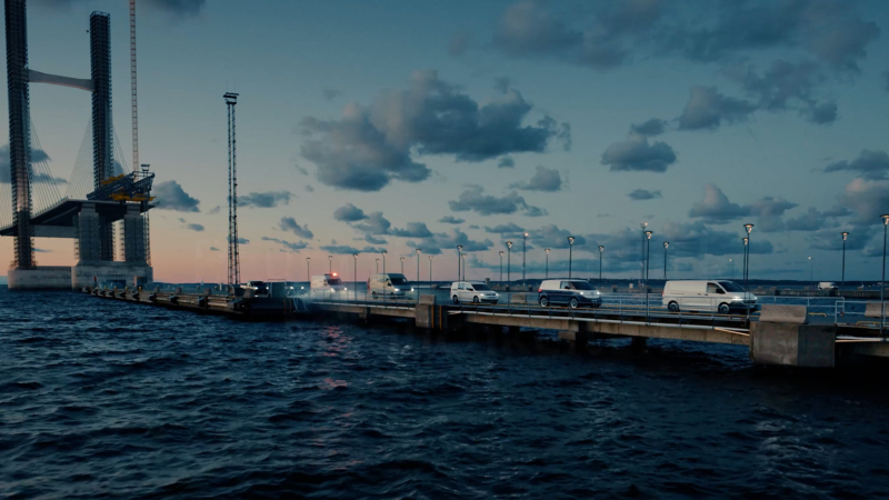 Eine Reihe von Volkswagen Nutzfahrzeugen auf dem Heimweg von einer Baustelle an einer Brücke.
