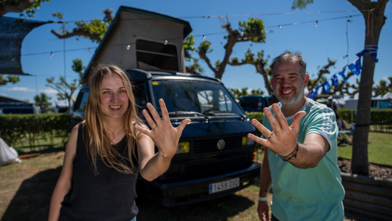 Una mujer y un hombre mostrando sus anillos de compromiso delante de un VW T3.