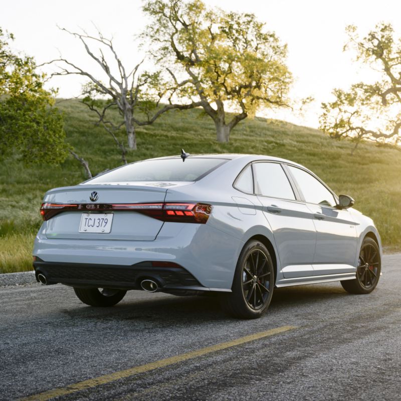 White Jetta GLI 2025 parked on a scenic road with trees and grassy hills in the background.