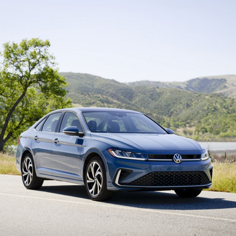 Front view of the blue 2025 Volkswagen Jetta showcasing its new exterior design with scenic hills in the background.