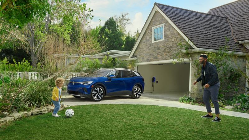 A father and son playing in the front yard with an ID.4 charging in the garage.