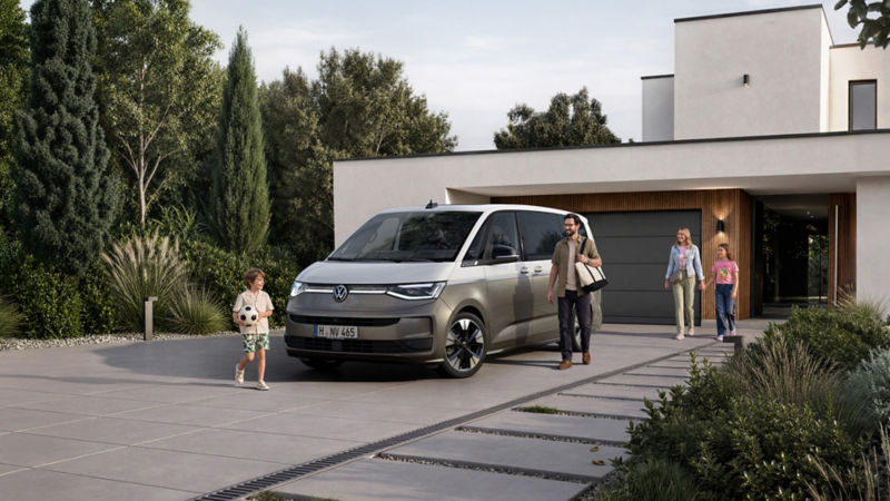 Volkswagen Multivan stationné devant une maison moderne. Plusieurs personnes se dirigent vers le véhicule sur l’allée, tandis qu’un enfant tient un ballon de football au premier plan.