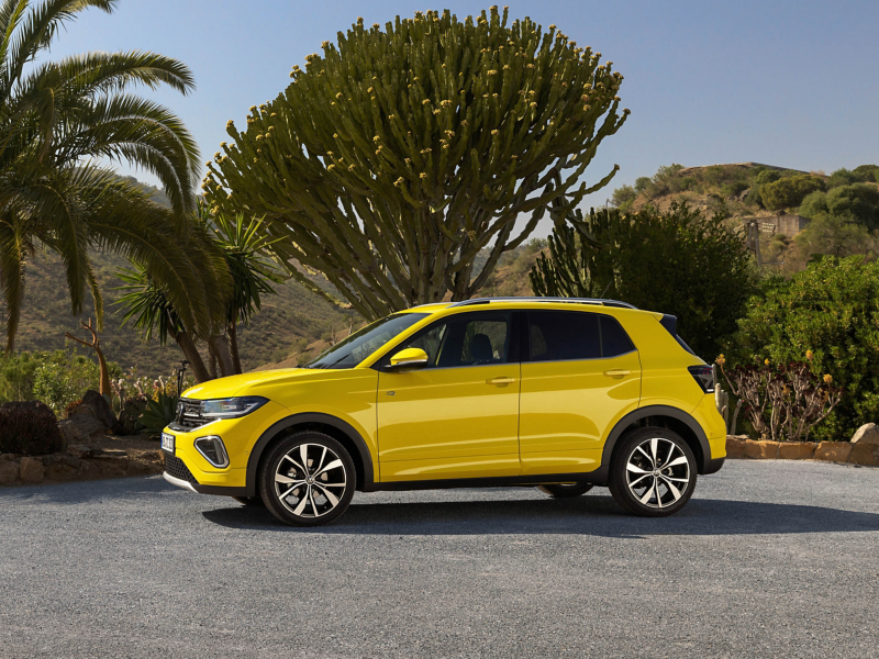 Bright yellow Volkswagen SUV parked on a sunny day with tropical trees and rolling hills in the background.