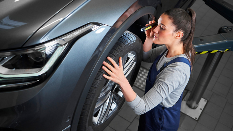 VW service employee checks the tyres of a VW Tiguan Allspace with a lamp