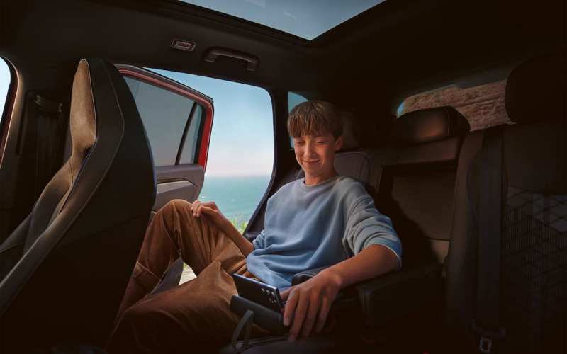 Jongen zit op de achterbank van een Volkswagen Tiguan, hij zit op zijn telefoon