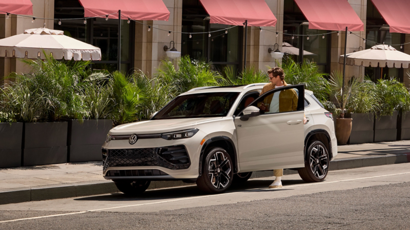 Man stepping out of a white SUV parked along a stylish city street with greenery, highlighting modern design and urban lifestyle.