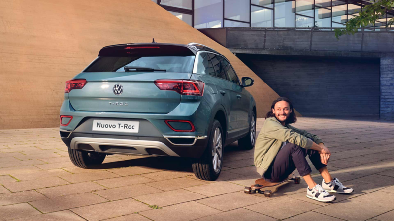 Vista 3/4 posteriore di Nuovo T-Roc parcheggiato con uomo seduto a fianco