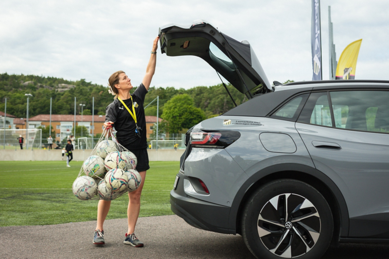 Fotbollstränare Ulrika Videli håller ett nät med fotbollar och stänger bakluckan på en Volkswagen ID.