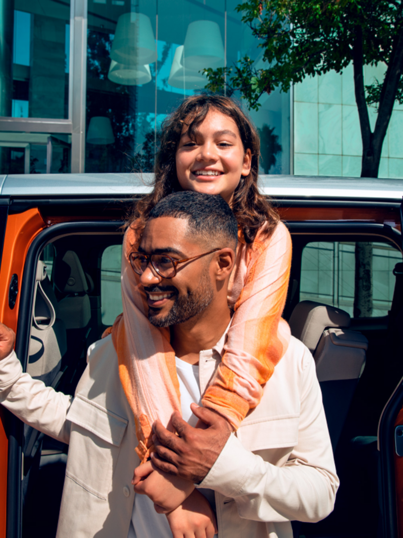 Un hombre con una niña subida a su espalda, saliendo de un vehículo VW.