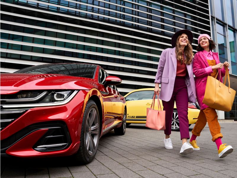 Mujeres comprando y paseando junto a vehículos Volkswagen.