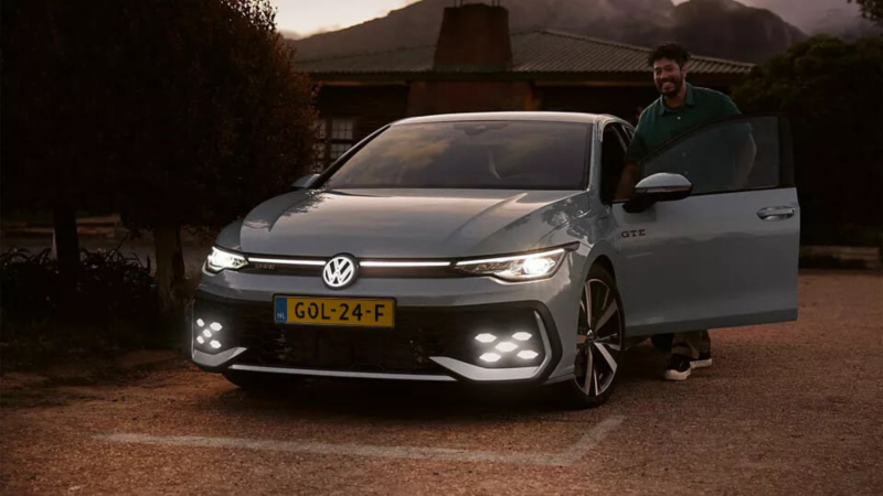 Man staat in de deuropening van een Grijze Golf GTE met verlichting in
