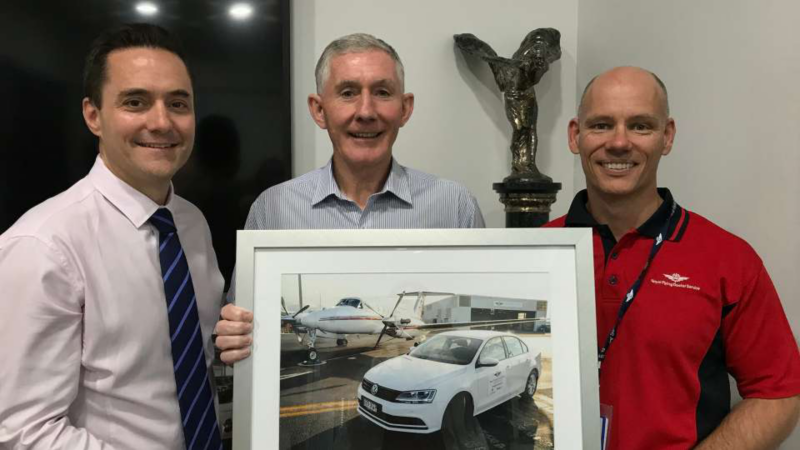 Three men stood holding framed image