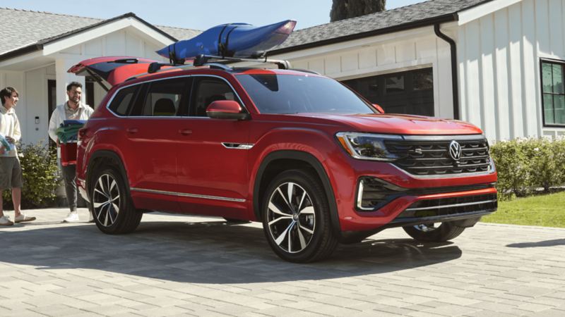 Two men load the trunk of a red Volkswagen Atlas