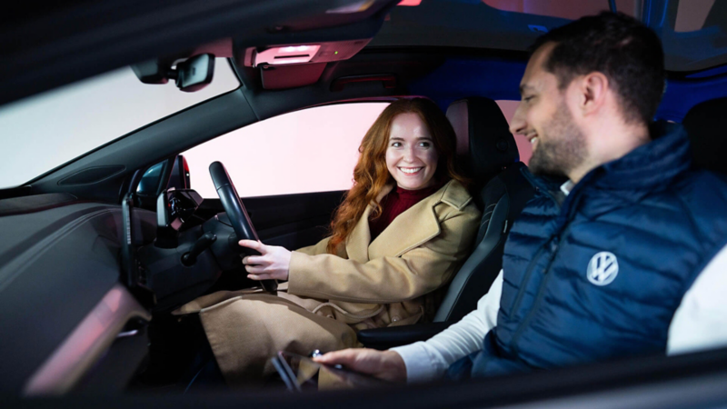A woman in the driver's seat of a VW smiling at a repair technician in the passenger's seat