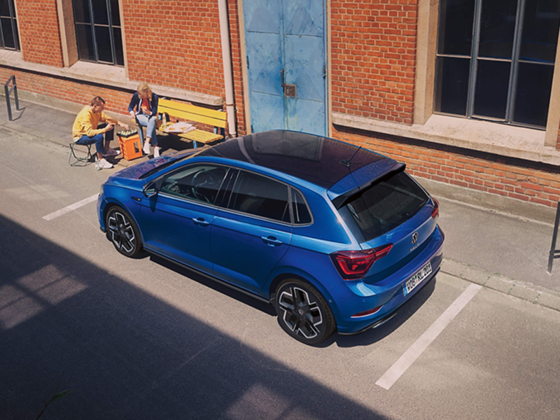 A blue Volkswagen Polo parked outside an old brick building