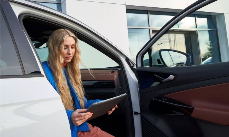 Woman sitting in Volkswagen vehicle using a tablet.