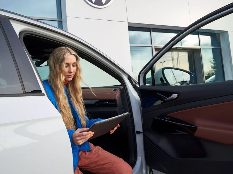 Mujer sentada en un vehículo Volkswagen usando una tableta.