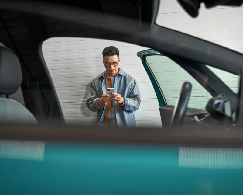 A young man opening his new car looking at his cell phone