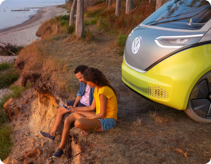 Pareja sentada junto a un vehículo eléctrico mirando al océano.