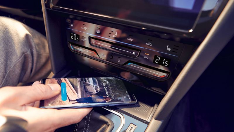 Passat telephone interface "Comfort", one hand places a smartphone in the compartment for inductive charging, the We Connect Home screen can be seen on the smartphone's display