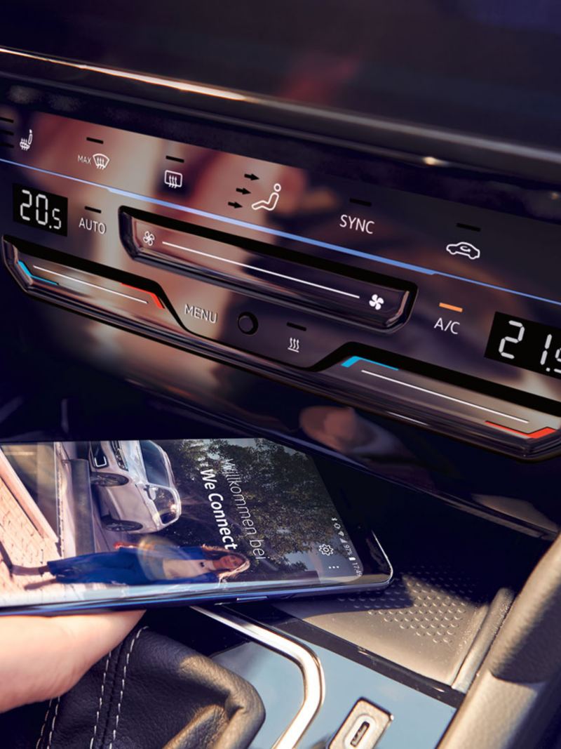 Passat telephone interface "Comfort", one hand places a smartphone in the compartment for inductive charging, the We Connect Home screen can be seen on the smartphone's display