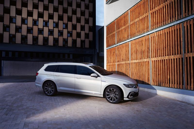 Vue arrière de la VW Passat GTE Berline et vue avant de la Passat GTE Variant l’une à côté de l’autre sur une place de stationnement, femme d’affaires quittant le parking pour se rendre dans un immeuble