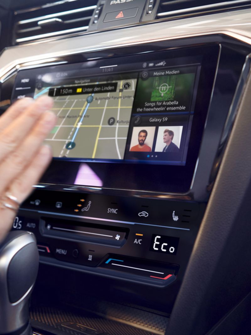 Detailansicht des optionalen Navigationssystems „Discover Media“ im VW Passat Variant. Eine Hand bewegt sich zum Touchscreen.