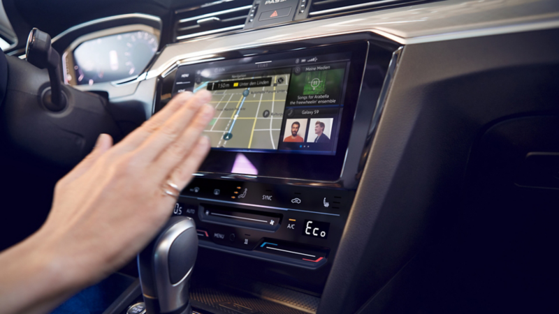 Nærbillede af navigationssystemet Discover Media (ekstraudstyr) i VW Passat Variant. En hånd bevæger sig mod bilens touchscreen.