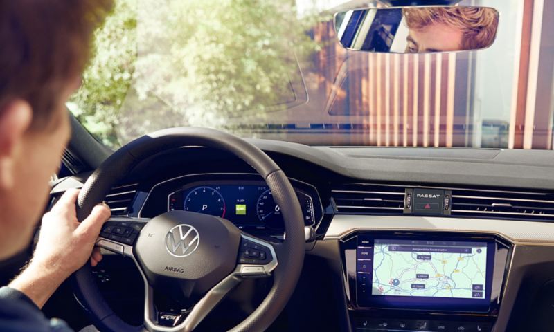 Vista interna della VW Passat Estate. Vista del conducente, del passeggero anteriore e dell'abitacolo con sistema di navigazione opzionale e volante multifunzione.