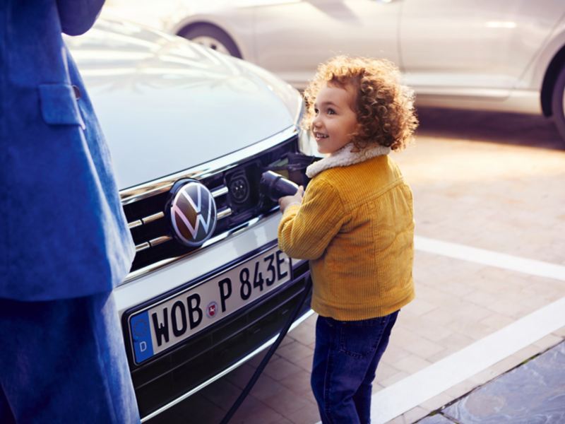 bambina inserisce connettore nella spina frontale auto VW ibrida plug in