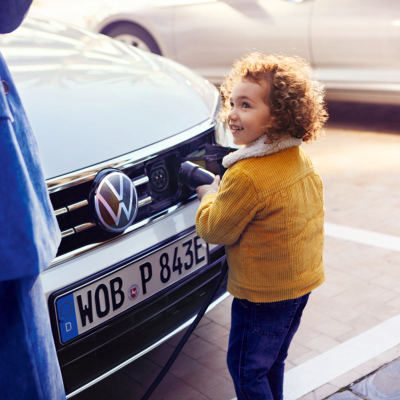 bambina inserisce connettore nella spina frontale auto VW ibrida plug in